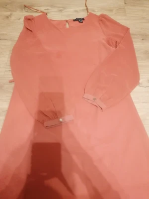 Ljusrosa långärmad kort klänning från Atmosphere - Söt ljusrosa klänning från Atmosphere i storlek 34. Klänningen har långa ärmar med knappdetalj vid mudden och en enkel, rak passform. Tillverkad i ett lätt och luftigt material som känns skönt mot huden. Den är kort. 