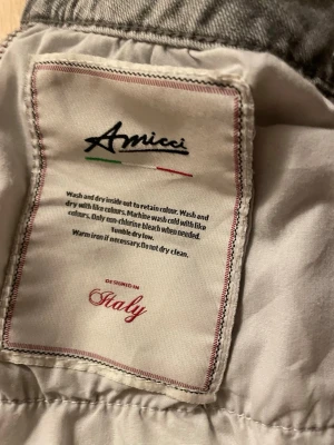 Grå jeans från Amicci, storlek 36 - Säljer ett par grå jeans från Amicci, designade i Italien. Byxorna har skinny passform och coola slitningar samt färgstänk för en edgy look. Klassisk femficksmodell med knapp och dragkedja i midjan. Perfekt för dig som gillar streetstyle.
