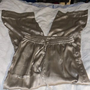 Beige blank  pyjamas set i polyester - Säljer en beige pyjamas från Lager157  i polyester material med mjuk glansig finish. Byxan  har knytband i midjan och en enkel, stilren design utan mönster. Perfekt för dig som gillar en clean look och vill ha något som känns lyxigt och bekvämt.