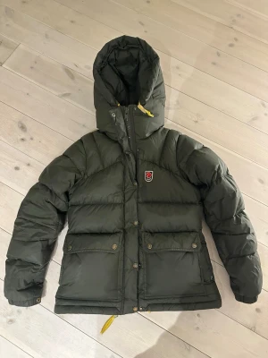 Fjällräven Expedition Down lite W - XS - Dags o sälja min fina Fjällräven jacka🌟 Jackan är i storlek XS dam, färgen deep forest (syns inte så bra på bilderna i ljuset). Det är alltså en av de ”nyare” modellerna. Köpte jackan vintern 2023 och den är välanvänd men fortfarande i fint skick. Dunet vid armvecken är aningen tunnare och överlag är den såklart inre lika flyffig som en nyinköpt, men märker ingen skillnad i utseende eller värme! Den har inga revor osv, se sista bild för aningen missfärgad ”plupp”😇 skriv privat för frågor/bilder!