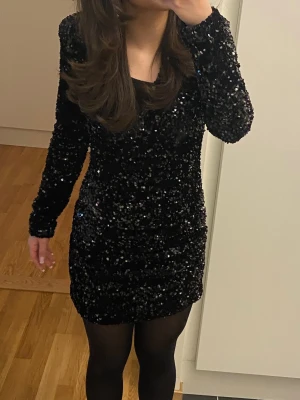 Nyårsklänning - Säljer en svart kort klänning från Gina Tricot, täckt med glittriga paljetter. Klänningen har lång ärm och v-ringad hals, vilket ger en snygg och festlig look. Köpt för 599kr och endast använt en gång💕