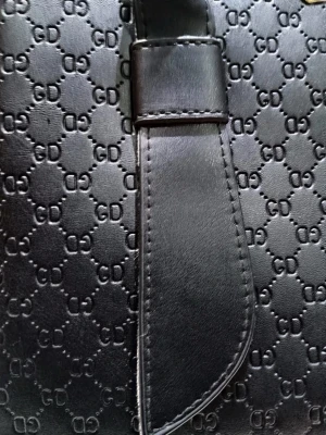 Svart handväska - Snygg svart handväska med präglat GD-mönster och guldfärgade detaljer. Väskan har två stadiga handtag, dragkedja på baksidan och dekorativa remmar framtill. Materialet är slätt skinnimitation och insidan är rymlig för dina grejer. Perfekt för dig som gillar stilrena accessoarer.