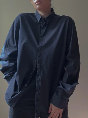 Vintage DKNY Black Cotton Shirt with Black Buttons - Vintage DKNY Black Cotton Shirt with Black Buttons. Excellent Condition. 96% cotton 4% elastane. Original Tagged size XL. Model is 160cm (5”3) and generally fits S/M.  68 CM/ 26.8 IN Length  66 CM/ 26 IN Sleeve  45 CM/ 17.7 IN Shoulders 110 CM/ 43.3 IN Chest   