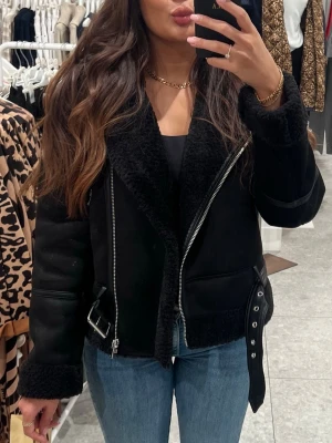 Svart bikerjacka från Stradivarius - Svart biker jacka från Stradivarius med detaljer i skinn och silverfärgade dragkedjor. Jackan har bred krage, bälte i midjan och mjukt teddyfoder både på insidan och vid ärmslut. Väldigt varm. Endast använd en gång!!! Helt som ny! Det går att vika ner ärmarna om man inte vill att teddymaterialet ska synas