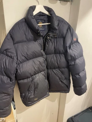 Morris R. Club Pufferjacka - Mörkblå pufferjacka från Morris R. Club. Den är i storlek L. Perfekt jacka för kalla dagar. Den är en gammal jacka så den har troligen mer värde.