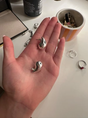 Silverfärgad droppformad väst - Säljer en unik väst i silverfärgat material med droppformad design. Västen har en slät och blank yta som ger ett coolt och modernt intryck. Perfekt för dig som gillar att sticka ut med din stil och vill ha något som känns annorlunda.