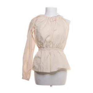 Beige omlott blus med oneshoulder - Säljer en beige blus med unik oneshoulder-design och omlott-detalj vid halsen. Toppen har en lång ärm på ena sidan och är ärmlös på andra, med smockad midja som ger en snygg siluett. Perfekt för dig som gillar statement-plagg med cool form.