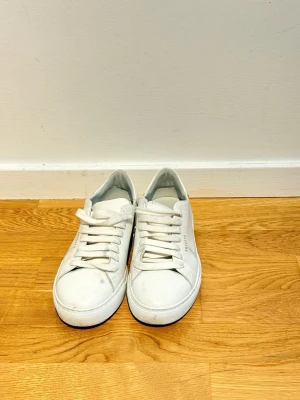 Vita sneakers från Axel Arigato - Säljer ett par stilrena vita sneakers från Axel Arigato med klassisk rund tå och platt sula. 