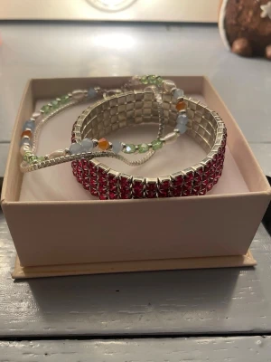 Armband - Bilderna visar två armband, ett rosa armband med rosa pärlor på och ett dubbelarmband med färgglada pärlor och en silver kedja. Kontakta ifall du är intresserad av ett armband istället för båda🤍