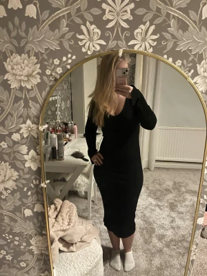 Svart ribbad långklänning - Säljer en svart långklänning med ribbad struktur och långärmade ärmar. Klänningen har en snygg v-ringad hals, slits vid ärmarna och är figurnära i modellen. Materialet är mjukt och stretchigt.