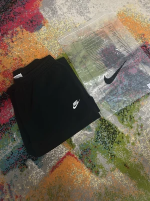 Svarta mjukisbyxor från Nike, storlek S - Svarta mjukisbyxor från Nike med klassisk logga i vitt på vänster lår. Byxorna har elastisk midja och är tillverkade i mjukt bomullsmaterial. Passformen är loose och de har raka ben. Perfekta för chill eller träning.