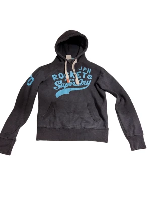 Mörkblå Superdry hoodie med tryck - Snygg trendig mörkblå hoodie från Superdry med ljusblå tryck på bröstet och ärmen. Skicka gärna frågor eller funderingar, pris kan ofta diskuteras.