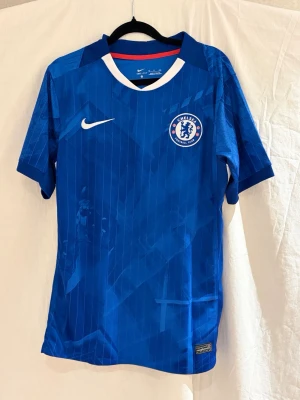 Chelsea Nike fotbollströja blå - Chelsea FC matchtröja i blått med vita och röda detaljer. Tröjan har klubbmärke på bröstet, Dri-Fit material och tryck med namn och nummer 41 på ryggen. Snyggt randigt mönster och klassisk rund hals med vit kant.