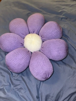 Lila stickad blomkudde - Superfin handgjord blomformad kudde med lila stickade kronblad och en vit stickad mitt. Kudden är mjuk och har en unik design som verkligen sticker ut i rummet. Perfekt som dekor på sängen eller soffan för att ge lite extra färg och mysig vibe.