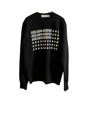 Svart sweatshirt från Golden Goose - Svart sweatshirt från Golden Goose med vit text och stjärnmönster på bröstet. Den är mjuk, varm och superbekväm perfekt att ha under kalla vinterdagar. Passar lika bra till vardags som när du vill vara lite extra snygg utan att anstränga dig.