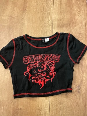 Svart croppad topp med röd print  - Svart tröja med röd text