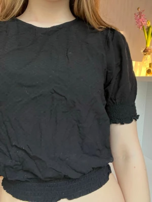 Svart blus med detaljer i 146/152 cm - Säljer eftersom blusen är på tok för liten för mig, Blusen ska inte vara så kort i magen som på bilden. Blusen är i tunt tyg med fina detaljer♥️
