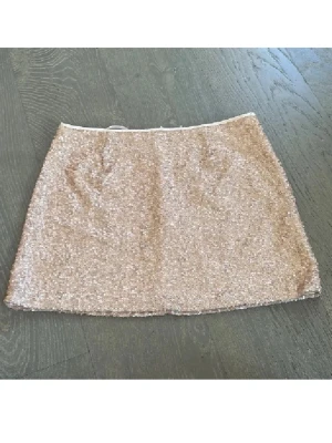 Festkjol💕 - Säljer en kort kjol från Jeane Blush i storlek M, täckt med glittriga paljetter i en champagnefärgad ton. Kjolen har rak passform och dragkedja bak. Perfekt för dig som vill sticka ut med lite extra bling och shimmer.