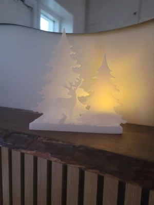 Vinterlandskap med ren & granar - ljusdekoration - ❄️✨ Vinterlandskap med ren & granar – ljusdekoration  Låt vintern flytta in i hemmet med denna magiska lilla ljussiluett 🦌🌲  En ståtlig ren står bland snötäckta granar – och när du tänder ett LED-ljus bakom motivet sprider sig ett varmt, mjukt sken som skapar riktig vintermagi.  Perfekt i fönstret, på hyllan eller som mysig detalj på julbordet. En enkel men elegant dekoration som passar i alla hem och sprider lugn, ljus och julkänsla.  ✨ Handgjord känsla ✨ Vit siluett med snödekor ✨ Endas för LED