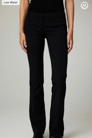 Svarta lågmidjade kostymbyxor - Snygga svarta kostymbyxor med låg midja och klassisk bootcut-silhuett. Byxorna har en stilren look med diskreta fickor och stängning fram. Perfekta för dig som gillar en clean och tidlös stil. Fåtal gånger använda 