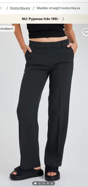 Svarta straight kostymbyxor - Svarta kostymbyxor från Maddie med rak passform och klassiska bälteshällor. Byxorna har en stilren design med pressveck framtill och är tillverkade i ett mjukt material som ger en snygg siluett. Perfekta för en clean och modern look.