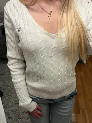 Vit tröja från GANT - Säljer en vit stickad tröja från GANT med kabelstickat mönster och v-ringad hals. Använd fåtal gånger. 