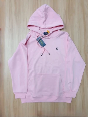 Rosa hoodie från Polo Ralph Lauren - Snygg ljusrosa hoodie från Polo Ralph Lauren med klassisk huva och snörning. Tröjan har en broderad logga på bröstet, stor magficka och ribbade muddar vid ärmslut och nederkant. Perfekt för chill dagar och enkel att matcha med jeans eller joggers. Storlek M men sitter som S, säljer då den är för liten och har inte kunnat använda den