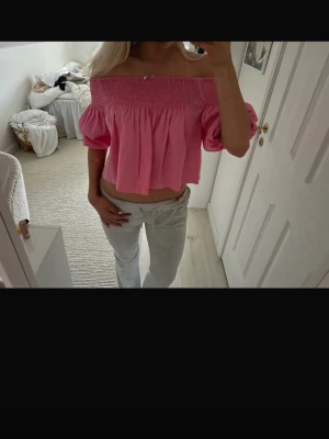 Rosa offshoulder croppad blus - Säljer en söt rosa blus med offshoulder och puffiga korta ärmar. Toppen är croppad och har smock upptill som ger en snygg passform över axlarna. Perfekt för varma dagar och har en luftig känsla. Materialet känns lätt och bekvämt.