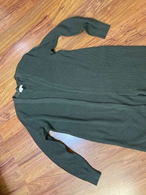 Mörkgrön lång cardigan jacka H&M - Säljer en mörkgrön, ribbad och lång cardigan jacka från H&M i storlek S. Jackan är stickad med långärmade ärmar och har en öppen front utan knappar eller dragkedja. Perfekt för lager-på-lager och chill stil.