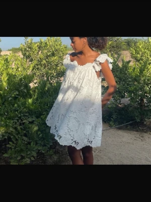 Vit spetsklänning med volangärmar - Superfin vit kortklänning i spets med blommigt mönster och volangiga axelband. Klänningen har en luftig och loose passform, perfekt för varma dagar. Söt och romantisk stil med v-ringning och detaljerade kanter. Ingen synlig dragkedja eller knappar.