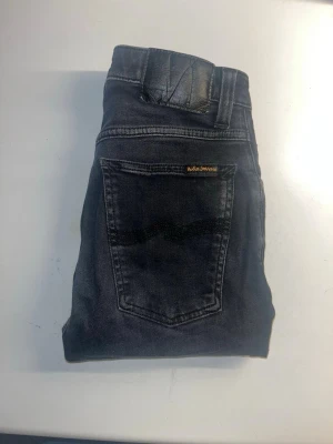 Nudie Jeans - Säljer ett par svarta skinny jeans från Nudie Jeans. Materialet är mjukt denim med stretch för extra komfort. Midja 31cm, längd 104cm. JAG SKICKAR EJ FLER BILDER NÄR JAG BÄR JEANSEN! för storleksguide hänvisar jag till måtten och för bättre inblick i passformen rekommenderar jag att googla på modellnamnet. kolla måtten noggrant :) s5,1