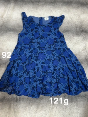 Blå blommig klänning - Supersöt blå klänning från Polarn o pyret med stora blommor i olika blå nyanser. Klänningen har ärmlös design med volangdetaljer vid axlarna och ett lätt, svängigt tyg som ger en lekfull look. Perfekt för sommarens alla äventyr!🌸 Fint använt skick. Storlek 104  