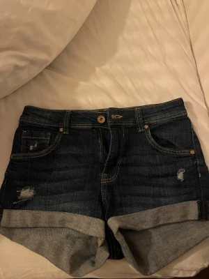 Mörkblå jeansshorts från Bershka - Säljer ett par mörkblå jeansshorts från Bershka i storlek 36. Klassisk femficksmodell med uppvikta benslut och slitna detaljer framtill. Perfekta till sommaren och har en snygg casual vibe. Frakten betalas av köparen.