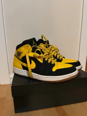 Nike Air Jordan 1 Mid svart/gul - Säljer ett par Nike Air Jordan 1 Mid i svart och gul med vita sulor. Skorna har klassisk snörning, svart mocka och gult skinn, samt ikoniska Jordan-loggor på sidan och hälen. Perfekta för dig som vill sticka ut med en färgstark sneaker.