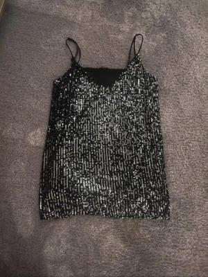 Svart glitter topp från new yorker  - Säljer ett snyggt svart glitter linne från new yorker. Snygg v-ringning och rak passform. Supersnygg till både jeans och kjol!