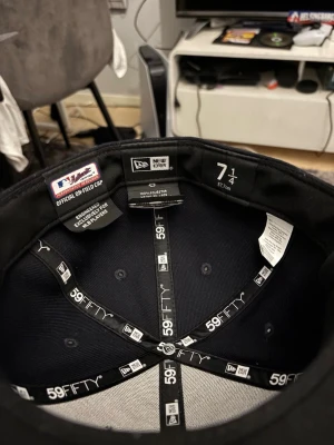 Boston Red Sox 59FIFTY keps New Era - Säljer en klassisk svart 59FIFTY keps från New Era med Boston Red Sox logga broderad i rött och vitt framtill. Kepsen är tillverkad i 100% polyester och har MLB-logga bak samt New Era-logga på sidan. Perfekt för dig som vill ha sportig stil.