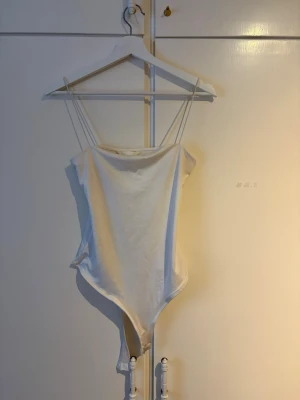 Vit body med tunna band från H&M - Säljer en enkel och stilren vit body från H&M i storlek S. Bodyn har tunna axelband och rak urringning, vilket ger en clean och modern look. Perfekt att styla med jeans eller kjol för en fräsch outfit☺️ Bodyn har nopper på flera ställen, finns på sista bilden att se💕