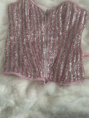 Glittrig rosa korsett - Supersnygg korsett i rosa och silver med glittriga paljetter och ränder. Figurnära modell som ger en riktigt statement look. Perfekt för dig som älskar glitter.