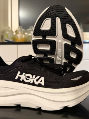 Hoka Bondi 9 löparskor svart/vit - Säljer ett par Hoka Bondi 9 löparskor i svart med vit tjock sula. Skorna har ventilerande mesh-ovandel, snörning och en riktigt chunky plattform för maxad komfort. Perfekta för dig som vill ha grym dämpning och stilren look till träningen.