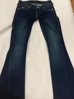 True Religion Joey Low Rise Flare Jeans - Säljer dem här helt nya Mörkblå jeans från True Religion, modell Joey Low Rise Flare för att jag inte han lämna tillbaka och va missnöjd hur dem satt på MIG. Snygga kontrastsömmar i gult och orange, klassiska fickor med lock och stora dekorativa sömmar bak. Bootcut/flare passform och låg midja. Tillverkade i slitstarkt denimtyg.