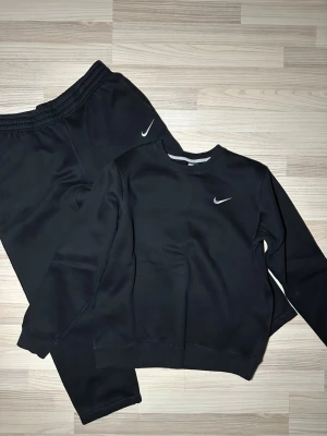 Svart Nike sweatshirt med logga - En stilren svart sweatshirt från Nike med klassisk vit swoosh-logga på bröstet. Tröjan har rund halsringning och ribbade muddar vid ärmar och nederkant. Perfekt för dig som gillar enkel och sportig stil. Liten i storleken 