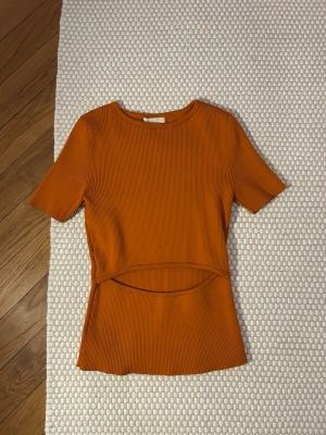 Ribbad orange topp med cut out - Säljer en ribbad orange topp i stretchigt material med korta ärmar och rund has från HM. Toppen har en snygg cut out-detalj framtill