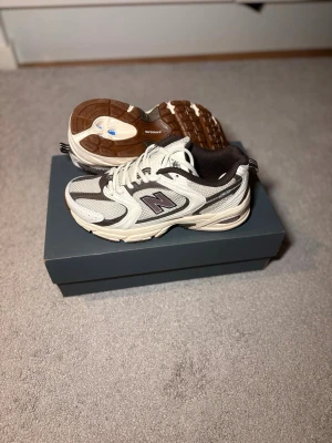 New Balance 530 sneakers vit/brun - Säljer ett par New Balance 530 sneakers i vitt och brunt med mesh och syntetpaneler. Klassisk chunky sula och tydlig logga på sidan. Skorna har snörning och en sportig vibe som passar till många olika stilar.