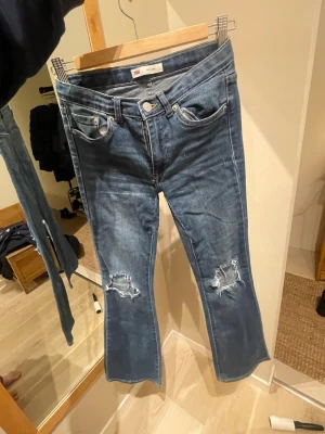 Levi's 726 Flare blå jeans - Säljer ett par Levi's 726 Flare jeans i klassisk blå tvätt. Jeansen har slitna detaljer vid knäna, fem fickor och flare-ben. De har normal passform och är tillverkade i tåligt denimtyg med dragkedja och knapp framtill. Har gjort hålen själv och även sytt dom lågmidjade men de har dock gått upp lite 