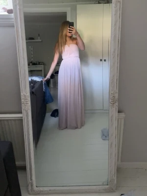 Ljusrosa balklänning - Supersnygg ljusrosa långklänning med axelbandslös design och draperad överdel. Klänningen har en flowy kjol och markerad midja, klänningen har gummi vid bysten göst upp så att den fäster bättre på kroppen och inte faller ner. perfekt för speciella tillfällen som till exempel BAL!! Materialet känns lätt och faller fint. jag är 169 cm lång. ❤️