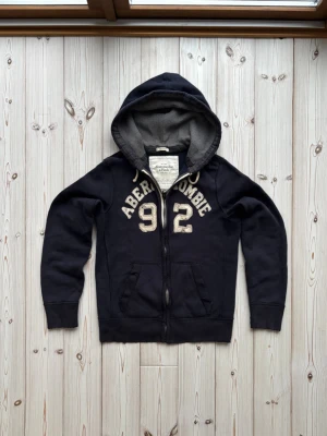 Abercrombie and fitch kofta - Säljer nu denna riktigt snygga och sällsynta vintage Abercrombie and fitch koftan i riktigt bra skick. Slitningarna på tröjan är en del av vintage looken. Storlek: M. Pris: 899kr. Skriv vid frågor eller för mer bilder! 🤩