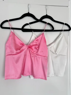 2st linnen i satin i rosa och vitt, storlek S - Två toppar i satin - rosa och vit. Mycket tunna axelband och lätt glansiga. Perfekt till jeans eller kjol. Använda en gång. Säljes tillsammans - men om du endast önskar köpa en av dem kan det också ordnas <3