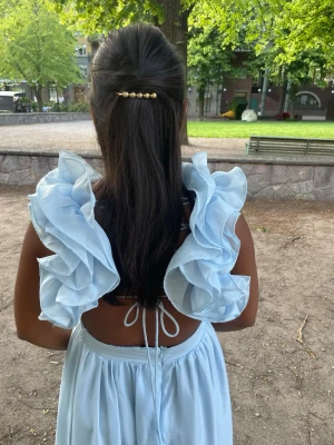 Ljusblå långklänning med snygg volang på axel - Säljer en ljusblå långklänning med volangaxelband och v-ringning. Klänningen har öppen rygg med knytband och volang i kjolen. Perfekt för 9:ans bal eller student och längden passar om du är ca 1.60 cm. 