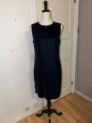 Mörkblå sammetsklänning Stockh LM - Snygg mörkblå kortklänning från Stockh LM i mjuk sammet. Klänningen är ärmlös med rund halsringning dekorerad med svarta pärlor. Stilren och elegant passform som ger en klassisk look. Perfekt för dig som gillar att sticka ut med enkla detaljer.