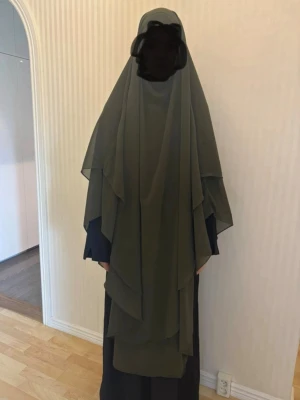 Olivgrön omlottkhinar i chiffong - Säljer en olivgrön omlott khimar med flera lager och flowig känsla. Khimaren har en lång och lös passform som täcker axlar och rygg. 